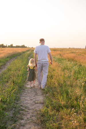 Dad and his blonde daughter are walking and having fun in a chamomile field.の写真素材