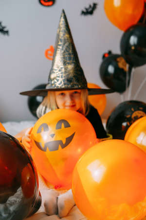 Childrens Halloween - a girl in a witch hat and a carnival costume with airy orange and black balloons at home. Ready to celebrate Halloween.の写真素材