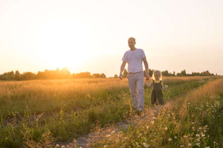 Dad and his blonde daughter are walking and having fun in a chamomile field.の写真素材