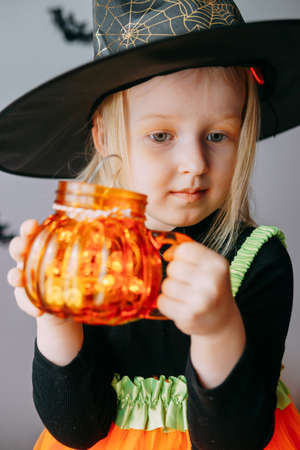 Childrens Halloween - a girl in a witch hat and a carnival costume with airy orange and black balloons at home. Ready to celebrate Halloweenの写真素材