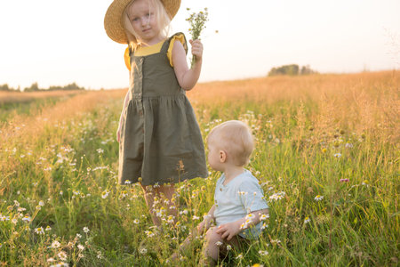 A little boy and a girl are picking flowers in a chamomile field. The concept of walking in nature,...