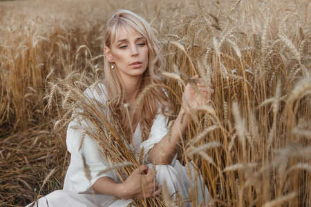 A blonde woman in a long white dress walks in a wheat field. The concept of a wedding and walking in natureの写真素材