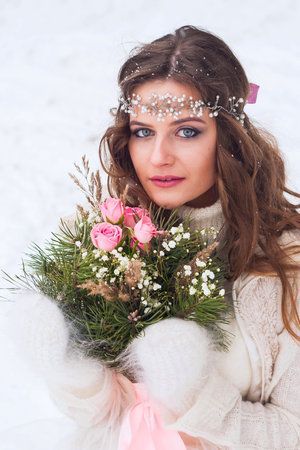 Beautiful bride in a white dress with a bouquet in a snow-covered winter forest. Portrait of the bride in nature.の写真素材