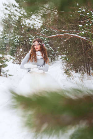 Beautiful bride in a white dress with a bouquet in a snow-covered winter forest. Portrait of the bride in nature.の写真素材