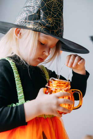 Childrens Halloween - a girl in a witch hat and a carnival costume with airy orange and black balloons at home. Ready to celebrate Halloweenの写真素材
