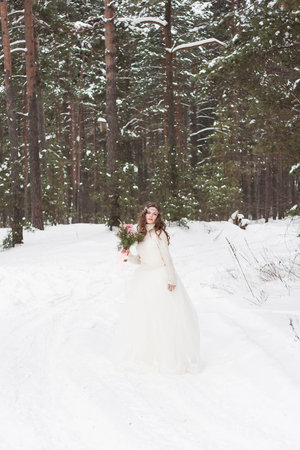 Beautiful bride in a white dress with a bouquet in a snow-covered winter forest. Portrait of the bride in natureの写真素材