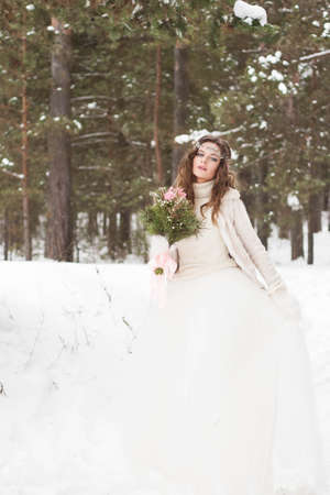 Beautiful bride in a white dress with a bouquet in a snow-covered winter forest. Portrait of the bride in natureの写真素材