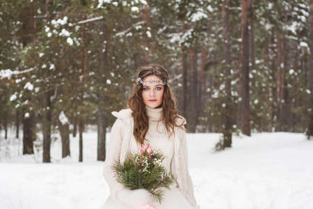 Beautiful bride in a white dress with a bouquet in a snow-covered winter forest. Portrait of the bride in natureの写真素材