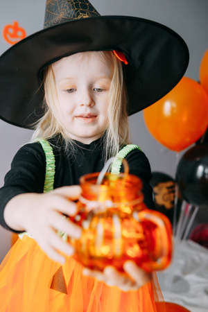 Childrens Halloween - a girl in a witch hat and a carnival costume with airy orange and black balloons at home. Ready to celebrate Halloweenの写真素材