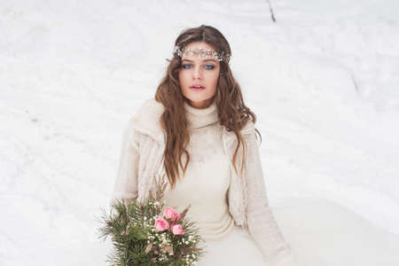 Beautiful bride in a white dress with a bouquet in a snow-covered winter forest. Portrait of the bride in nature.の写真素材