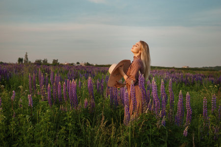 A beautiful woman in a straw hat walks in a field with purple flowers. A walk in nature in the lupin fieldの写真素材