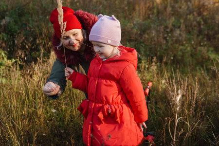 A little girl in a red coat walks in nature in an autumn grove with her grandmother. The time of the year is autumn.の写真素材