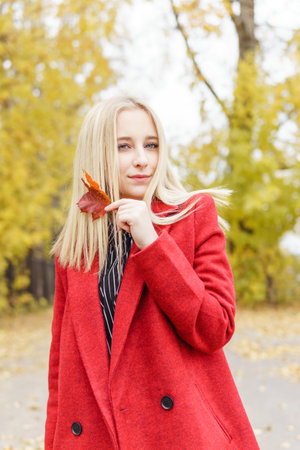 A young blonde woman walks around the autumn city in a red coat. The concept of urban style and lifestyleの写真素材