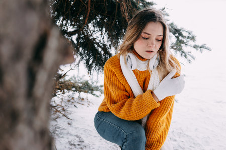Teen blonde in a yellow sweater outside in winter. A teenage girl on a walk in winter clothes in a snowy forestの写真素材