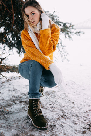 Teen blonde in a yellow sweater outside in winter. A teenage girl on a walk in winter clothes in a snowy forestの写真素材