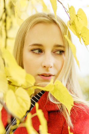 A young blonde woman walks around the autumn city in a red coat. The concept of urban style and lifestyle. Autumn portrait.の写真素材