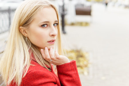 A young blonde woman walks around the autumn city in a red coat. The concept of urban style and lifestyleの写真素材