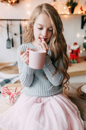 A blonde girl with long hair drinks cocoa from a pink cup with pleasure. Christmas atmosphereの写真素材