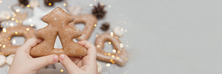 Childrens hands hold a gingerbread in the shape of a Christmas tree. The concept of Christmas sweets, toys, garlands and bokeh. Decor for New Year holidaysの写真素材