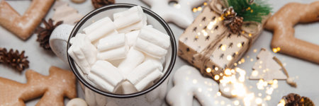 A cup of cocoa with marshmallows and New Years gingerbread and a gift on the table, bokeh lights in the foreground. The concept of desserts and drinks during the Christmas holidays.の写真素材