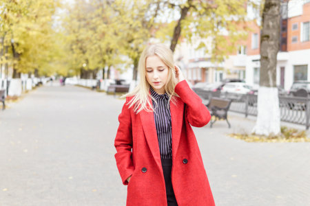 A young blonde woman walks around the autumn city in a red coat. The concept of urban style and lifestyleの写真素材