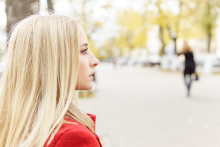 A young blonde woman walks around the autumn city in a red coat. The concept of urban style and lifestyleの写真素材
