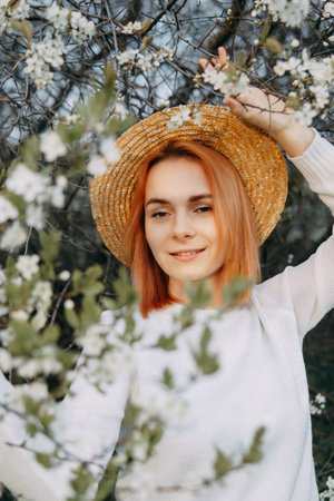Portrait of a woman in a straw hat in a cherry blossom. Free outdoor recreation, spring blooming garden.の写真素材