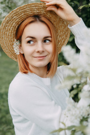 Portrait of a woman in a straw hat in a cherry blossom. Free outdoor recreation, spring blooming garden.の写真素材