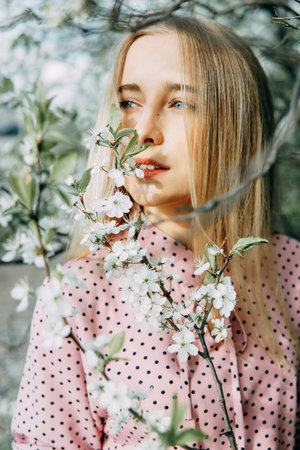 Blonde girl on a spring walk in the garden with cherry blossoms. Female portrait, close-up. A girl...