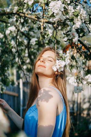 Beautiful young girl in a blue dress in a blooming Apple orchard. Blooming Apple trees with white flowers.の写真素材