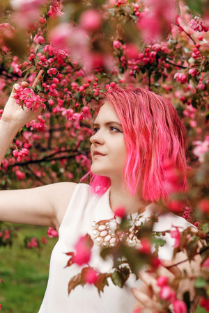 Young girl with pink hair in an Apple orchard. Beautiful young girl in a blooming garden of pink...