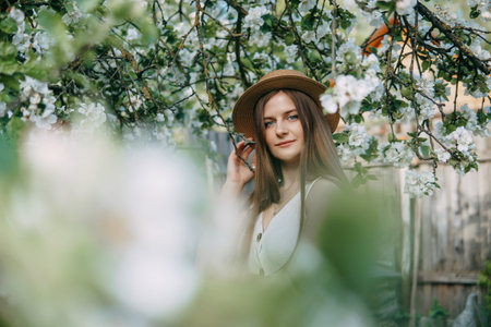 Beautiful young girl in white dress and hat in blooming Apple orchard. Blooming Apple trees with white flowers.の写真素材