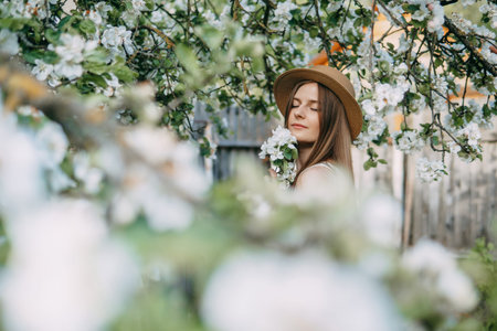Beautiful young girl in white dress and hat in blooming Apple orchard. Blooming Apple trees with...