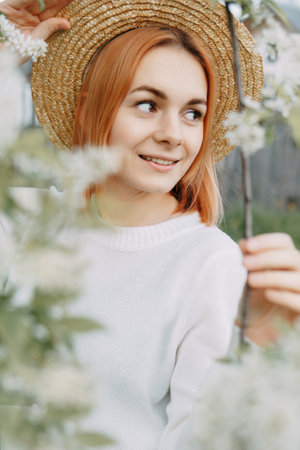 Portrait of a woman in a straw hat in a cherry blossom. Free outdoor recreation, spring blooming garden.の写真素材