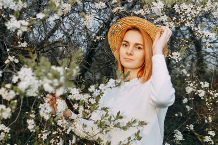 Portrait of a woman in a straw hat in a cherry blossom. Free outdoor recreation, spring blooming garden.の写真素材
