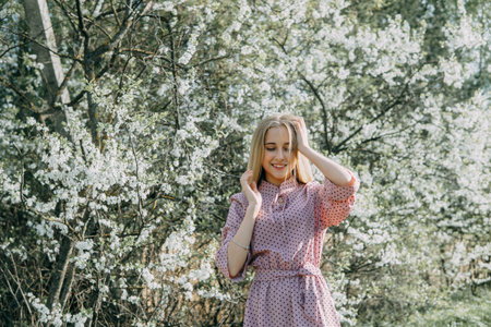 Blonde girl on a spring walk in the garden with cherry blossoms. Female portrait, close-up. A girl...