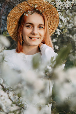 Portrait of a woman in a straw hat in a cherry blossom. Free outdoor recreation, spring blooming garden.の写真素材