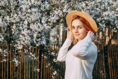 Portrait of a woman in a straw hat in a cherry blossom. Free outdoor recreation, spring blooming garden.の写真素材