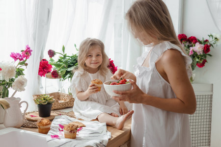 A little blonde girl with her mom on a kitchen countertop decorated with peonies. The concept of the relationship between mother and daughter. Spring atmosphere.の写真素材
