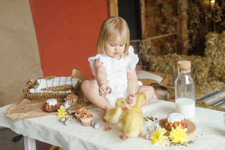 A little girl is sitting on the Easter table and playing with cute fluffy ducklings. The concept of celebrating happy Easter.の写真素材