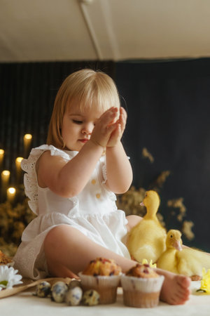 A little girl is sitting on the Easter table and playing with cute fluffy ducklings. The concept of...