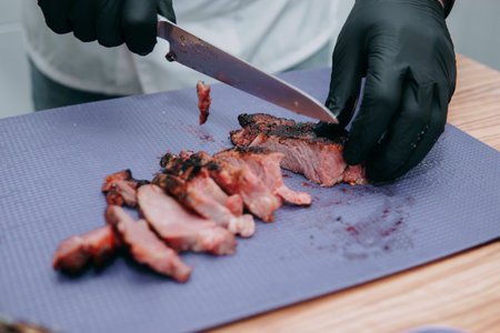 Cutting Beef steak. Cook in black gloves cuts beef steak on a cutting Board. Cooking class on cooking steaks.の写真素材