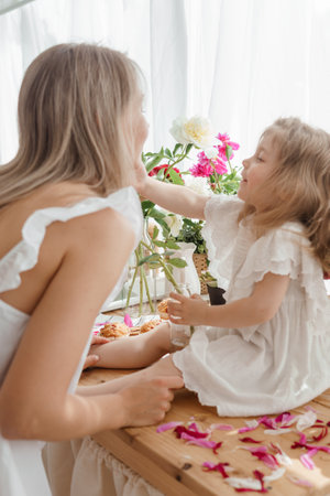 A little blonde girl with her mom on a kitchen countertop decorated with peonies. The concept of the relationship between mother and daughter. Spring atmosphere.の写真素材