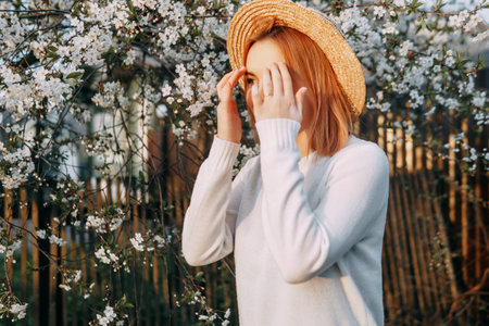 Portrait of a woman in a straw hat in a cherry blossom. Free outdoor recreation, spring blooming garden.の写真素材