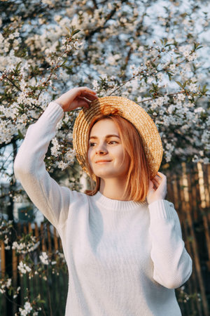 Portrait of a woman in a straw hat in a cherry blossom. Free outdoor recreation, spring blooming garden.の写真素材