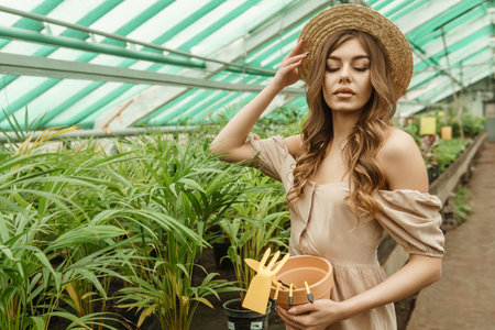 A beautiful young woman takes care of plants in a greenhouse. The concept of gardening and an eco-friendly lifestyle.の写真素材