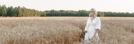 A blonde woman in a long white dress walks in a wheat field. The concept of a wedding and walking in natureの写真素材