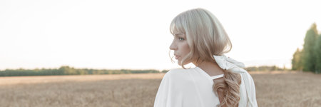 A blonde woman in a long white dress walks in a wheat field. The concept of a wedding and walking in nature.の写真素材
