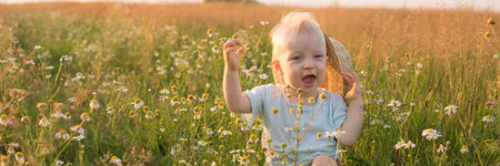 A little blond boy is sitting in the grass in a chamomile field. The concept of walking in nature, freedom and an environmentally friendly lifestyleの写真素材