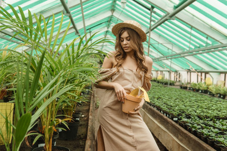 A beautiful young woman takes care of plants in a greenhouse. The concept of gardening and an eco-friendly lifestyle.の写真素材